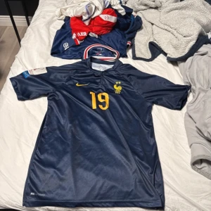 Blå fotbollströja med nummer 19 - Säljer en blå fotbollströja från Nike med nummer 19 och namn på ryggen. Tröjan har korta ärmar och ett gult tryck på framsidan. Perfekt för fotbollsfans! Pris kan diskuteras 