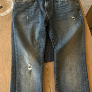 Blå jeans med slitningar - Snygga blå jeans med slitningar på framsidan för en trendig look. De har en klassisk femficksdesign och en läderpatch baktill. Perfekta för en avslappnad stil.