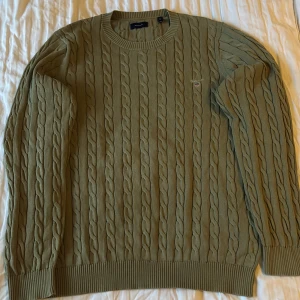 Grön kabelstickad tröja från Gant - Säljer en snygg grön kabelstickad tröja från Gant. Den har en klassisk design med rund hals och ribbade muddar. Perfekt för höst och vinter, och den är i mycket bra skick. Passar både till vardags och lite finare tillfällen. Skick 9/10, knappt använd. Storlek Xl men sitter som L
