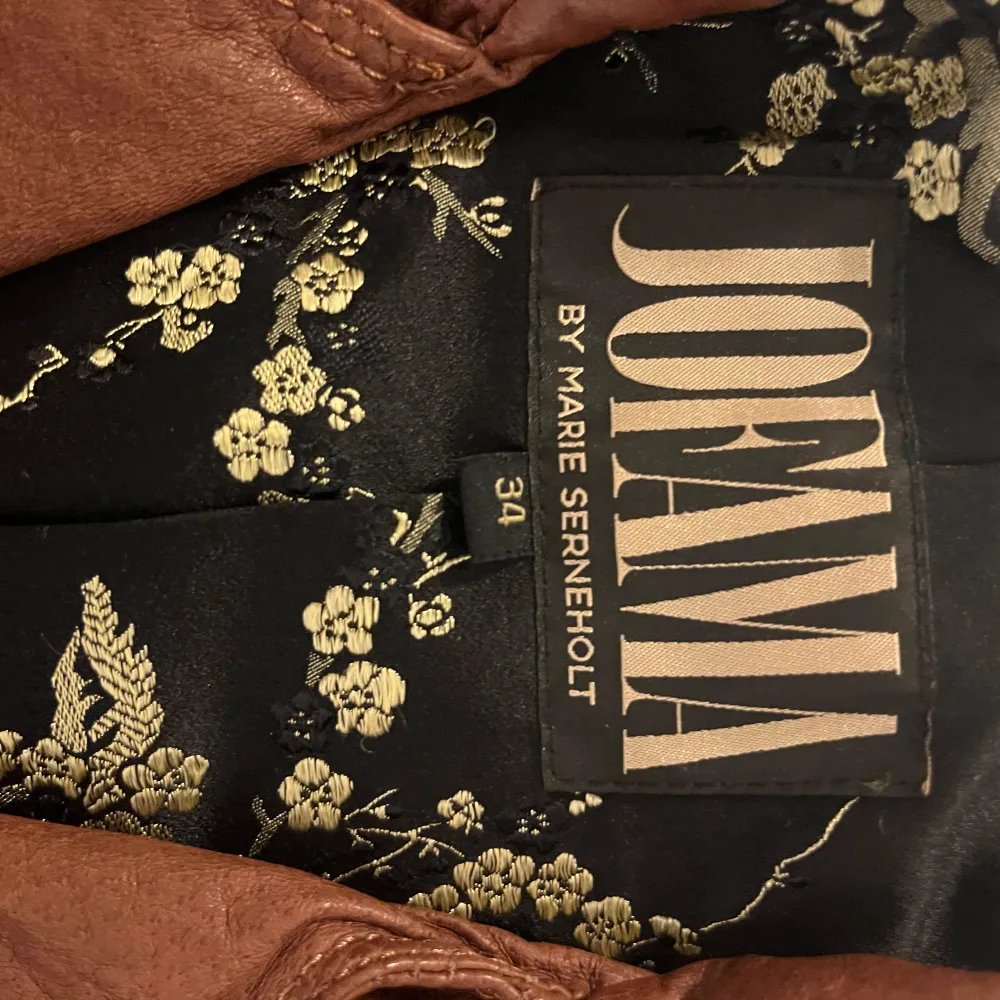 Snygg brun skinnjacka från Jofama designad av Marie Serneholt. Jackan har en dragkedja framtill och stiliga detaljer med knappar. Perfekt för en cool och trendig look.. Takit.