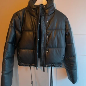 Svart pufferjacka  - Snygg svart pufferjacka med dragkedja och knappar. Jackan är croppad och har långa ärmar. Perfekt för kyliga dagar med stil. Ej använd 