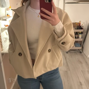 Beige kappa med knappar från missäy  -  beige kappa med stora knappar och bred krage. Jackan har en croppad design och långa ärmar. Från missäy i storlek s. Aldrig använd så inga defekter eller liknanade. Nypris 500
