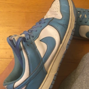 Nike Dunk i blått och vitt - Säljer ett par Nike Dunk sneakers i blått och vitt. Skorna har en klassisk design med snörning och en bekväm passningsform, dom är dock lite cresade vilket syns på bilden men fortfarande väldigt sköna