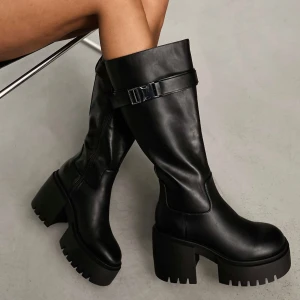 Svarta boots med spänne - Snygga svarta boots i skinn med kraftig klack och spänne upptill. Perfekta för en trendig look med sin robusta design och höga skaft. Köpt från ASOS original pris 789kr och slutsålda. Använda bara ett par gånger.