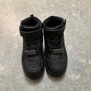 Svarta Marvel sneakers med spindelnätsmönster - Coola svarta sneakers med hög design och spindelnätsmönster från Marvel. Skorna har snörning och kardborreband för extra säker passform. Perfekta för alla Marvel-fans! Använd en gång. passar till barn