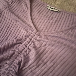 Lila ribbad topp - Säljer en lila ribbad topp med korta ärmar och knytning framtill. Perfekt för en avslappnad stil.