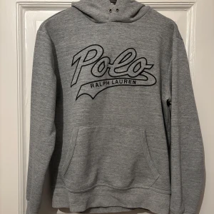 Grå Ralph Lauren Hoodie - Säljer en sällsynt grå hoodie från Ralph Lauren med stor Polo-logga på framsidan. Skick: 8/10. Inga tecken på slitning som syns vid användning, har en mindre defekt på insidan, be om bild. Fråga på!