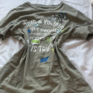 Olivgrön t-shirt från Zadig & Voltaire - Cool olivgrön t-shirt från Zadig & Voltaire med tryck i flera färger på framsidan. Perfekt för en avslappnad stil med en touch av edge.