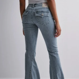 Blå jeans från True Religion - Snygga blå jeans från True Religion med bootcut och låg midja. De har dekorativa bakfickor med knappar. Dem är i modellen ”joey” och är i storlek 27. Säljer pga att de är alldeles för stora (jag har 34 i jeans i vanliga fall) Dem är använda två gånger och är i perfekt skick! Nypris: 1 299kr☺️