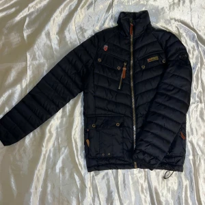Svart quiltad jacka från Geographical Norway -  Svart quiltad jacka från Geographical Norway med dragkedja och flera fickor. Jackan har en hög krage och i jättebra skick.