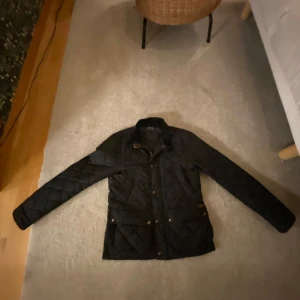 Svart quiltad jacka från Polo Ralph Lauren - Snygg svart quiltad jacka från Polo Ralph Lauren med långa ärmar och stilrena detaljer. Perfekt för kyligare dagar med sin klassiska design och bekväma passform. Jackan har knappar och en diskret krage. Odenarie pris ligger runt 3000 
