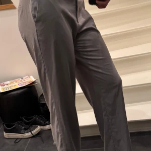 Grå kostymbyxor - Snygga grå kostymbyxor med medelhög midja och rak passform. Byxorna har en klassisk design med dragkedja och knapp framtill.