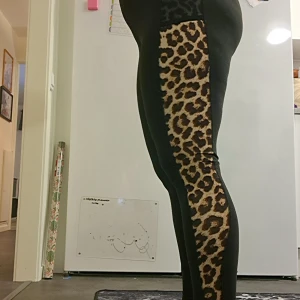 Svarta leggings med leopardmönster - Snygga svarta leggings med leopardmönstrade paneler längs sidorna. Perfekta för att ge en djärv touch till din outfit. De har en praktisk ficka på båda sidor och är tillverkade i ett stretchigt material för en bekväm passform.