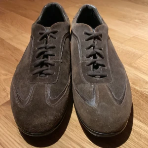 Lyxsneakers från Santoni - Hej, jag säljer dessa snygga bruna mockaskor från Santoni i nyskick med inga defekter och med en klassisk snörning. Skorna är i storleken 41 men passar 41,5. Skorna har en elegant design med en låg profil och är perfekta för en stilren look. Tillverkade i högkvalitativ mocka som ger en lyxig känsla. Om du har några funderingar är det bara att fråga och priset kan diskuteras. Skorna ingår bara.