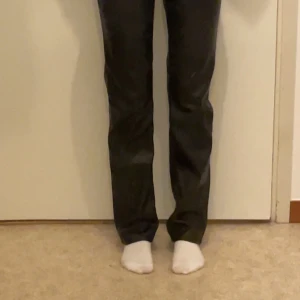 Svarta byxor i skinn från 157 - Snygga svarta byxor i skinnmaterial från 157. De har en tight passform och är lågmidjad med dragkedja och knappar framtill. Perfekta för en stilren look.