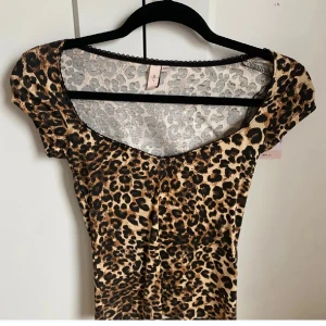 Leopardmönstrad tröja Nelly - Snygg leopardmönstrad topp från Nelly  med korta ärmar och en djup rund halsringning. Perfekt för att ge en vild touch till din outfit. 🐆