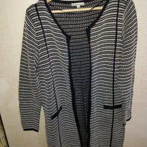 Svartvit mönstrad kappa från Samantha Levin - Snygg svartvit kappa från Samantha Levin med ett unikt mönster. Den har långa ärmar och en öppen design utan knappar eller dragkedja. Perfekt för att ge din outfit en stilren touch.