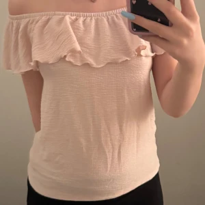 Rosa offshoulder topp med volang - Säljer en söt beige offshoulder topp med volangdetaljer. Perfekt för sommarens varma dagar. Toppen har en smickrande passform och är tillverkad i ett mjukt material.