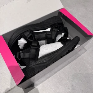 Svarta sandaler med kardborreband - Snygga svarta sandaler med justerbara kardborreband för perfekt passform. Sandalerna har en robust sula och är perfekta för sommarens äventyr. De är stilrena och bekväma, vilket gör dem till ett utmärkt val för både stad, strand och jobb. De är endast testade. Nypris 500 kr!