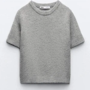 Grå stickad tröja från Zara - Säljer en stilren grå stickad tröja från Zara. Tröjan har korta ärmar och en rund halsringning, perfekt för lager-på-lager under kyligare dagar. Enkel och tidlös design som passar till det mesta.