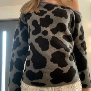 Grå och svart leopardmönstrad tröja - Snygg grå tröja med svart leopardmönster. Tröjan har en offshoulder-design som ger en trendig look. Perfekt för att sticka ut i mängden!