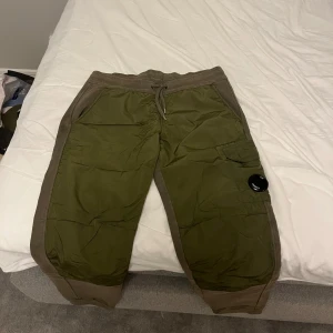 Gröna mjukisbyxor från cp company  - Säljer ett par gröna mjukisbyxor från C.P. Company. Byxorna har en bekväm passform med snörning i midjan och en ficka med en rund detalj på benet. Perfekta för en avslappnad stil. Storleken är 12 år men passar typ mig och jag är 15 och 184 lång. Skriv för bilder hur de sitter på mig