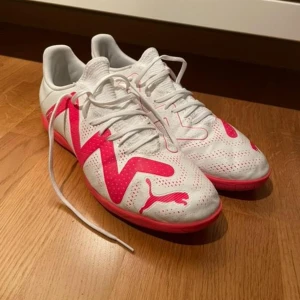 Inne fotbollsskor från Puma - Snygga vita fotbollsskor från Puma med rosa detaljer och snörning. Skorna har en perforerad ovansida för bättre ventilation och en greppvänlig sula för inomhusspel. Använd 2 gånger. 