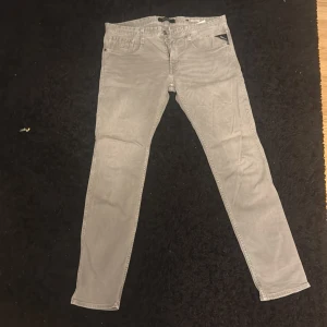 Grå jeans från Replay - Snygga grå jeans från Replay i modellen Anbass. De har en slim passform och är tillverkade i ett bekvämt jeansmaterial. Perfekta för en stilren look med klassiska femfickor och knappgylf.