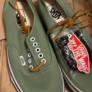 Gröna Vans sneakers - Snygga gröna Vans sneakers med vita detaljer och bruna snören. Skorna har en klassisk design med vit sula och Vans logotyp på sidan. Perfekta för en avslappnad stil. finns en defekt på framsidan bild 4