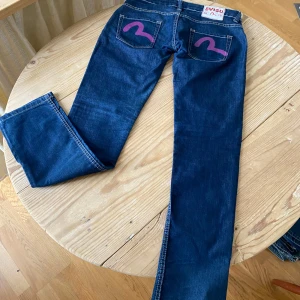 Y2k evisu super lowwaist bootcut jeans med lila print - Såå fina super lågmidjade evisu jeans med klassisk evisu logga/tryck i lila baktill på fickorna!! Slitsar längst ner i benen, ganska raka o lite bootcut i benen!! Midja 40cm, innerben 81cm, midja till gren 18cm  Vintage, 70tal,90tal, y2k, 2000s, boho chic, rock chic, Ibiza summer, glitter, strass, nitar, studs, rhinestones, bling, paljetter, western, cowboy, fringe, tassle, fransar, läder, genuine leather, suede, mocka, stockholmstyle, Stockholmsstil, wedge boots, marant, bohoo, zara, flowy, ava