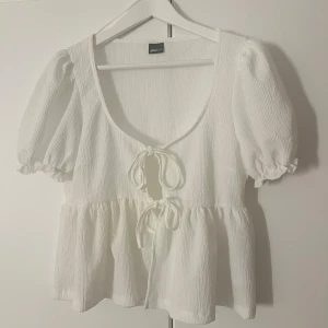 Vit blus med knytning - Säljer en söt vit blus från ginatricot med knytning framtill. Blusen har korta puffärmar och en luftig passform. Perfekt för varma dagar eller sommarens fester. 🕊️