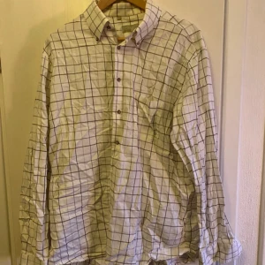 Rutig skjorta från Oscar - Säljer en klassisk rutig skjorta från Oscar i vitt med bruna och svarta rutor. Skjortan har långa ärmar och knappar framtill. Perfekt för en stilren look.