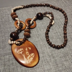 Unikt afrikansk halsband med trädetaljer - Unikt afrikansk amerikansk halsband med bruna och beige trädpärlor. Hänget har ett ingraverat blommotiv som ger en bohemisk känsla. Perfekt för att ge en naturlig touch till din stil. Längden är 40 cm.
