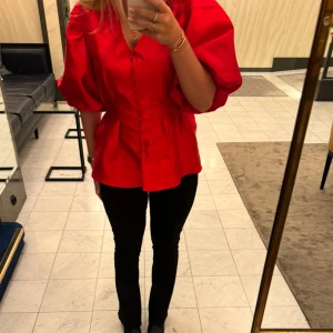 Aida Blouse By Malina - Aida Blouse från By Malina i färgen Cherry. Slutsåld i alla storlekar. Snygg röd blus med puffiga ärmar och knappar framtill. 