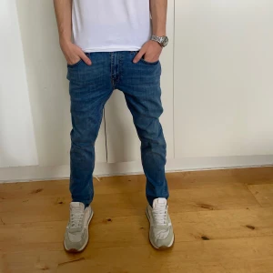 Blå jeans från tiger of sweden  - Snygga blå jeansbyxor med en slim passform (pistolero) De har en klassisk design med dragkedja och knappar. Perfekta för en avslappnad stil. Kom privat för fler bilder. Skick 9/10. Modellen är 177