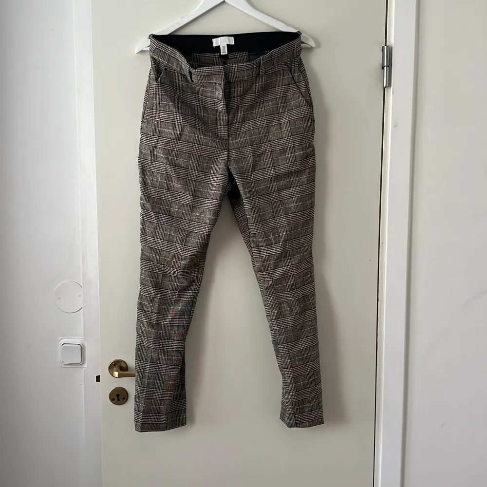 Snygga rutig byxor från H&M i svart och beige. Byxorna har en dragkedja och knappar framtill för enkel stängning. Perfekta för en stilren look.. Farkut & Housut.