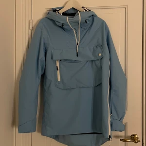 Ljusblå vindjacka med dragkedja - Snygg ljusblå snowboard/skidjacka. Jackan har en stor ficka framtill med knapp och dragkedja, perfekt för att förvara småsaker. Den är långärmad och har en stilren design som passar perfekt för blåsiga dagar.(stor i storleken, skulle passa s-m)