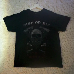 Svart t-shirt med tryck från Gildan - Cool svart t-shirt från Gildan med ett tufft tryck av en dödskalle med bandana och texten 'Ride or Die'. Tillverkad i tung bomull för en skön känsla. Perfekt för en edgy look.
