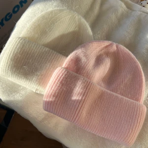 Rosa och vit stickad mössa - Två mysiga stickade mössor i rosa och vit färg. De har en ribbad design och är perfekta för kyliga dagar. Mössorna är mjuka och bekväma, vilket gör dem till ett stilrent val för vintern. 200kr/st 