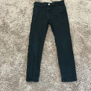 Svarta byxor från Grimaldi - Snygga svarta byxor från Grimaldi med dragkedja och knapp framtill. De har en klassisk design med normal passform och är perfekta för en stilren look. Byxorna är tillverkade i ett bekvämt material som passar till många olika tillfällen.