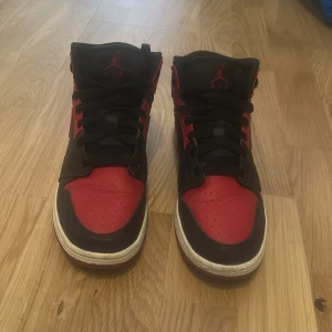 Nike Air Jordans i svart och röd - Snygga Nike Air Jordans i klassisk svart och röd färgkombination. Skorna har hög snörning och en ikonisk design med Nike-loggan på sidan. Perfekta för dig som vill ha en stilren och sportig look.