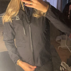 Svart Gore-Tex jacka från Haglöfs - Säljer en svart Gore-Tex jacka från Haglöfs, perfekt för regniga dagar. Jackan har dragkedja och är långärmad med en stilren design. Den är tillverkad i slitstarkt material och har en praktisk ficka med dragkedja på bröstet. 