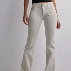 Vita bootcut jeans - Snygga vita bootcut jeans från Nelly (slutsålda) med låg midja och klassisk femficksdesign. Byxorna har en knapp och dragkedja framtill samt fickor med lock och knapp bak. Perfekta för en stilren look. Använda fåtal gånger och inga tecken på användning🫶🏼