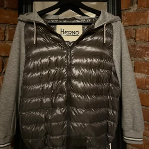 Grå cardigan från Herno  - Snygg grå cardigan från ett italienskt märke Herno. Cardiganens ny pris ligger runt 7000kr. Cardiganen har en fet dragkedja med bra kvalitet och en snygg huva, den har även fickor som gömmer sig snyggt i materialet och syns inte .Perfekt för en stilren look och sköna vår dagar