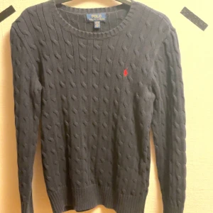 Mörkblå kabelstickad tröja från Ralph Lauren - Säljer en stilren mörkblå kabelstickad tröja från Ralph Lauren. Tröjan har en klassisk design med rund hals och ett diskret rött broderat märke på bröstet. Skulle säga att den passar en XS. Pris kan diskuteras 