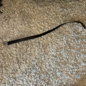 Svart bälte med silverfärgat spänne - Snyggt svart bälte med ett stilrent silverfärgat spänne. Perfekt för att komplettera din outfit. Bältet har flera hål för justering och är tillverkat i ett robust material. Pris kan diskuteras.