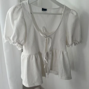 Vit blus med knytning - Charmig vit blus med korta puffärmar och knytning framtill. Blusen har en u-ringad design💕