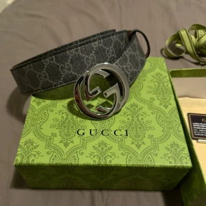 Gucci Bälte - Säljer ett stilrent grått bälte från Gucci med det klassiska GG-mönstret. Bältet har ett stort, glänsande silverfärgat spänne med Gucci-logotypen. Perfekt för att ge en lyxig touch till din outfit.