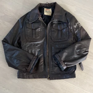 Brun skinnjacka från Replay - Säljer en snygg brun skinnjacka från Replay med dragkedja och broderad text på ärmen. Jackan har en klassisk krage och flera fickor framtill. Perfekt för en cool look!