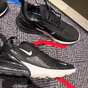 Svarta Nike sneakers - Snygga svarta Nike sneakers med vit sula och synlig Air-dämpning i hälen. Skorna har en modern design med snörning och små vita detaljer. Perfekta för en sportig look. Använda 3-4 gånger 